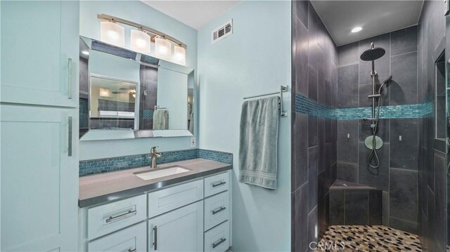 full bathroom with vanity, tiled shower, and visible vents