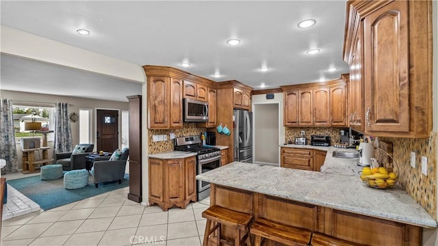 kitchen with a peninsula, light tile patterned floors, brown cabinetry, and stainless steel appliances