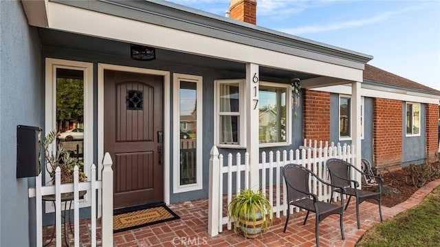 entrance to property with stucco siding, brick siding, a porch, and a chimney