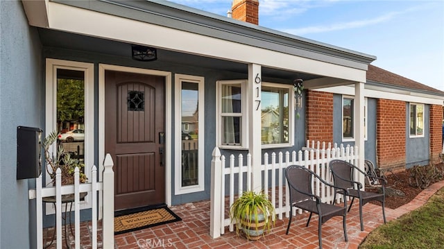entrance to property with fence, covered porch, a chimney, and brick siding