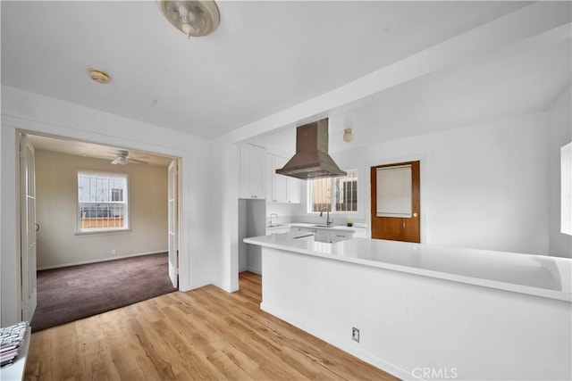 kitchen featuring white cabinets, island exhaust hood, light countertops, light wood-style floors, and a sink