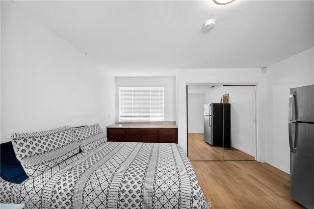 bedroom featuring freestanding refrigerator, a closet, baseboards, and light wood finished floors