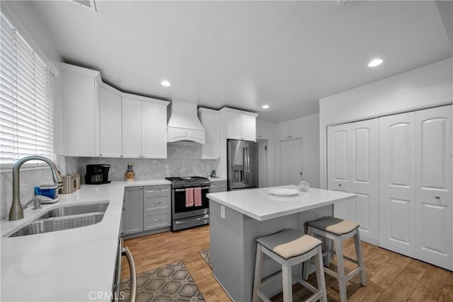 kitchen with light wood-style flooring, stainless steel appliances, a sink, custom exhaust hood, and a kitchen bar