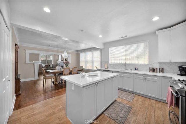 kitchen with visible vents, a kitchen island, light countertops, stainless steel range with gas cooktop, and a sink