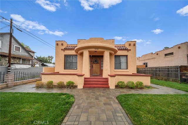 view of front of property with a front yard, a tile roof, fence, and stucco siding