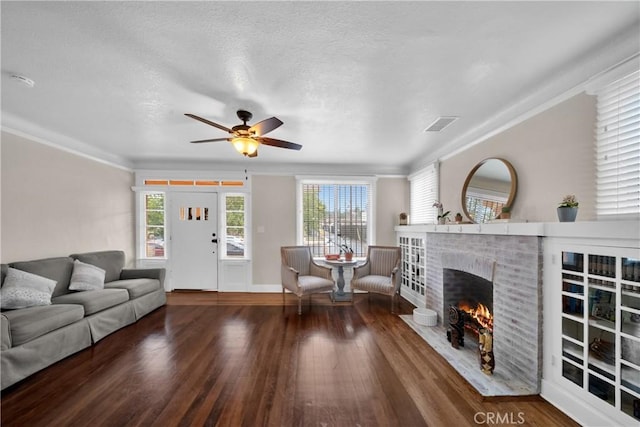 living area with a wealth of natural light, visible vents, a fireplace, and wood finished floors