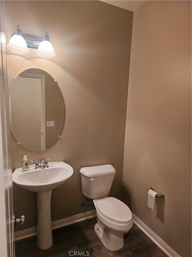 half bathroom featuring a sink, baseboards, toilet, and wood finished floors