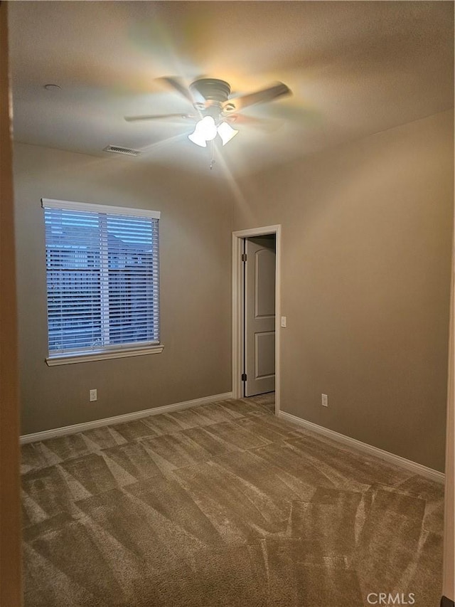 carpeted spare room featuring visible vents, baseboards, and ceiling fan