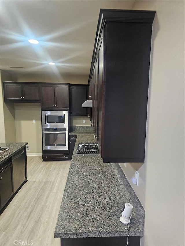 kitchen with recessed lighting, stainless steel appliances, dark stone counters, light wood-style floors, and dark brown cabinetry