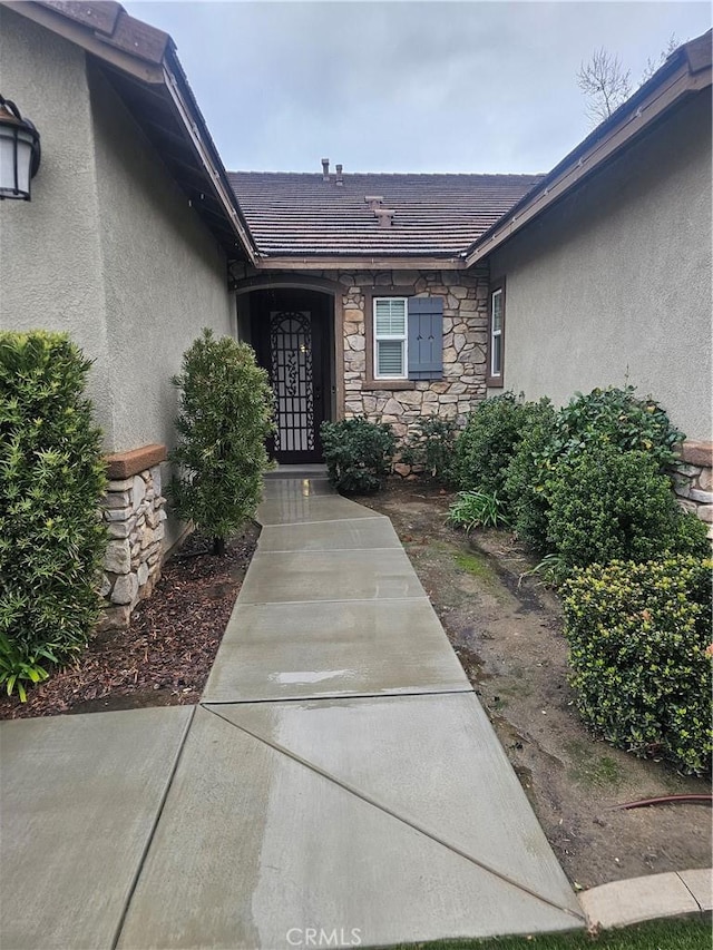 property entrance featuring stucco siding, stone siding, and a tile roof