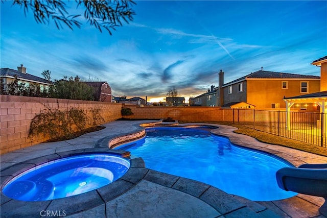 pool at dusk with a water slide, a fenced backyard, and a pool with connected hot tub