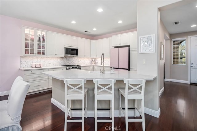 kitchen with visible vents, stove, stainless steel microwave, freestanding refrigerator, and a kitchen bar