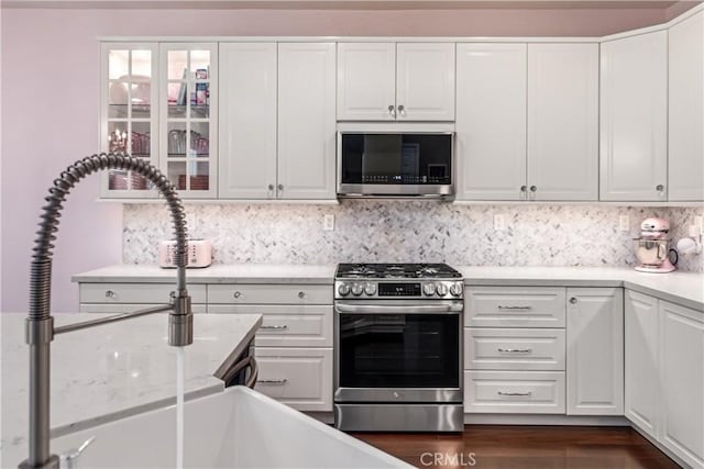 kitchen with white cabinetry, stainless steel appliances, backsplash, and light countertops