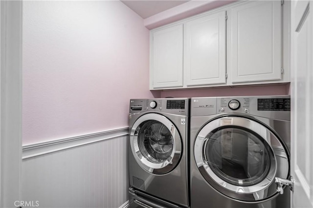 washroom featuring cabinet space, washing machine and dryer, and a wainscoted wall