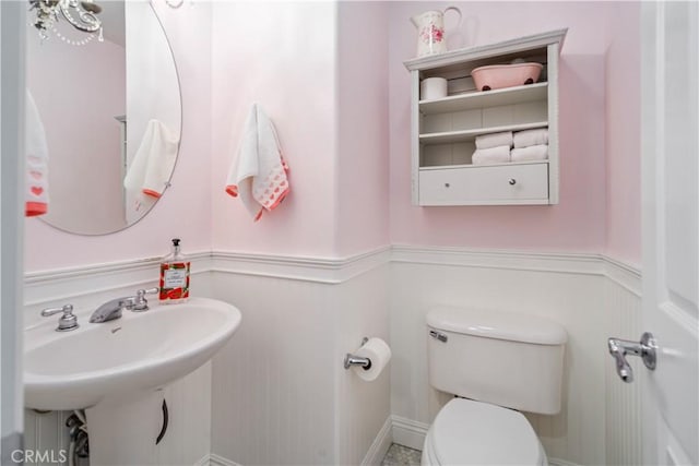 bathroom featuring a wainscoted wall, a sink, and toilet