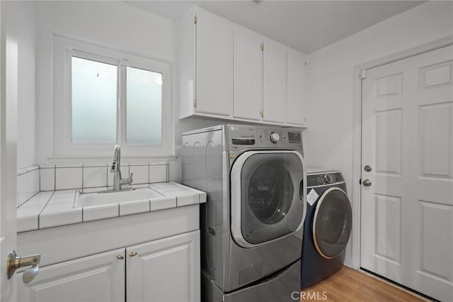 washroom featuring light wood-type flooring, cabinet space, a sink, and washing machine and clothes dryer