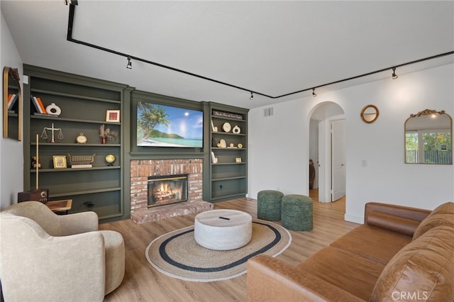 living area with a brick fireplace, track lighting, arched walkways, and wood finished floors