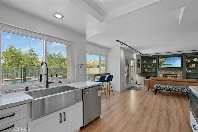 kitchen with light stone counters, light wood-style floors, a brick fireplace, a sink, and dishwasher