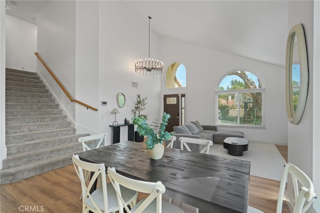 dining space featuring stairs, a high ceiling, a notable chandelier, and wood finished floors