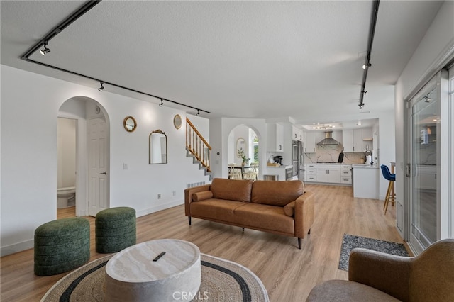 living room with arched walkways, light wood finished floors, and stairway