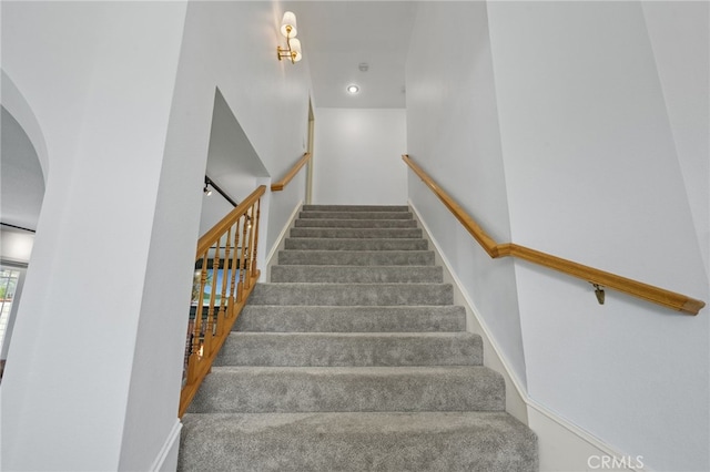 stairway with baseboards, arched walkways, and carpet flooring