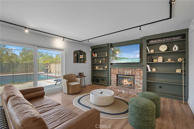 living room featuring track lighting, a fireplace, wood finished floors, and built in features