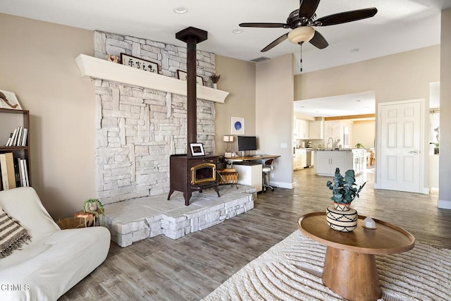 living area with a ceiling fan, a wood stove, wood finished floors, and visible vents