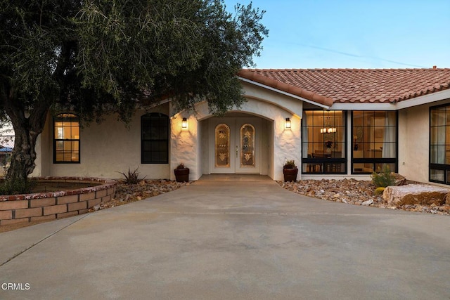 property entrance featuring french doors, concrete driveway, stucco siding, and a tile roof