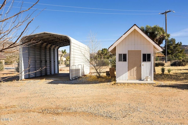 view of shed with a carport, fence, and dirt driveway