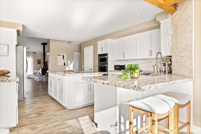 kitchen featuring black appliances, backsplash, a peninsula, white cabinets, and light wood finished floors