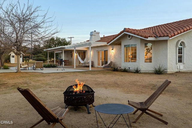 back of house featuring a tiled roof, stucco siding, a patio, and an outdoor fire pit