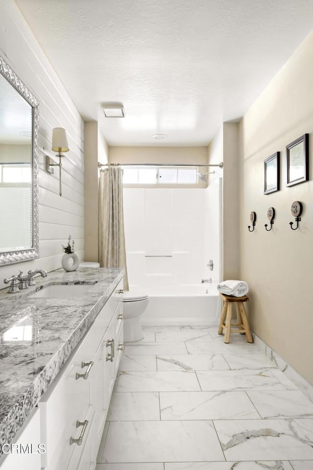 full bathroom featuring shower / bath combo with shower curtain, toilet, marble finish floor, a textured ceiling, and vanity