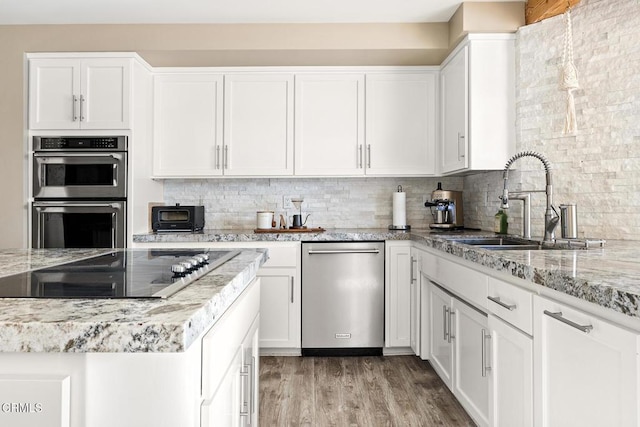 kitchen with tasteful backsplash, black electric stovetop, stainless steel double oven, white cabinets, and a sink