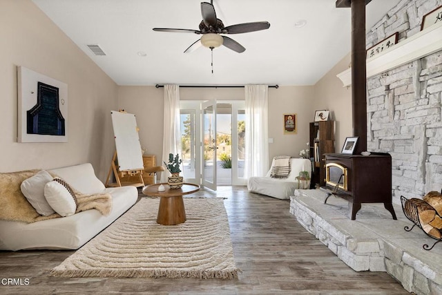 living room with visible vents, ceiling fan, vaulted ceiling, a wood stove, and wood finished floors