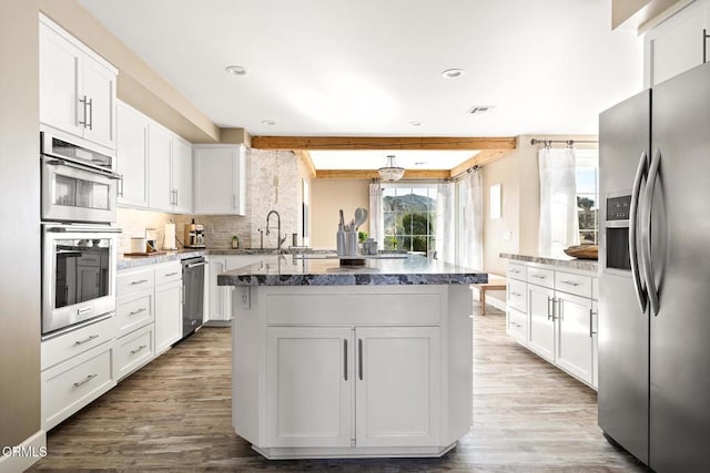 kitchen with dark stone counters, decorative backsplash, appliances with stainless steel finishes, wood finished floors, and white cabinets