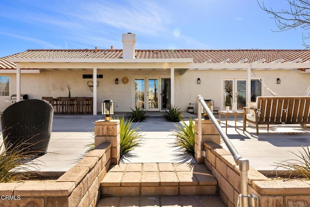 rear view of house with stucco siding, french doors, and a tile roof