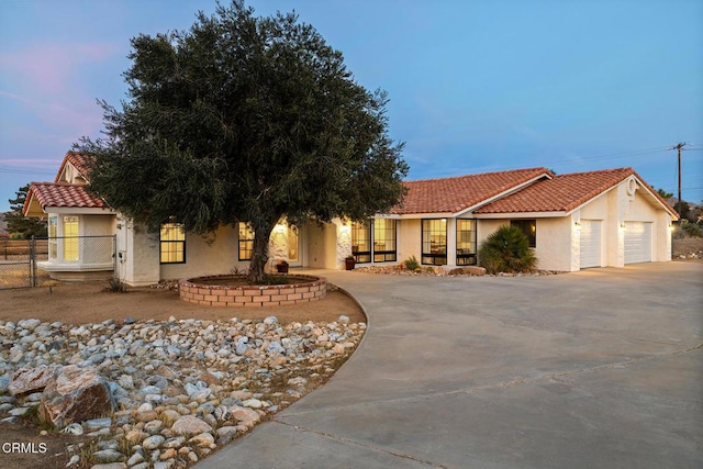 view of front facade with concrete driveway, a tiled roof, fence, and stucco siding