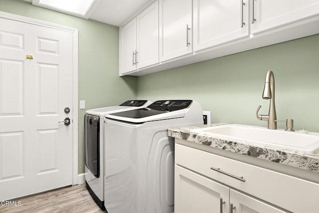 laundry room featuring washing machine and clothes dryer, cabinet space, light wood-type flooring, and a sink