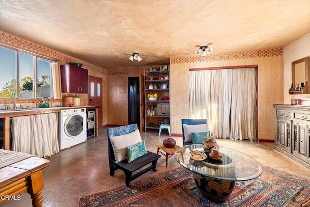 living area with finished concrete floors, washer / clothes dryer, baseboards, and wallpapered walls