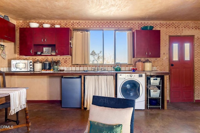 kitchen with concrete flooring, a sink, baseboards, washer / clothes dryer, and stainless steel fridge