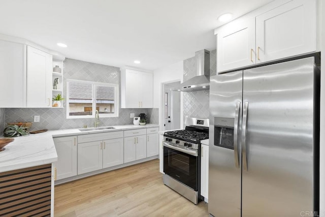 kitchen with white cabinets, a sink, appliances with stainless steel finishes, and wall chimney range hood