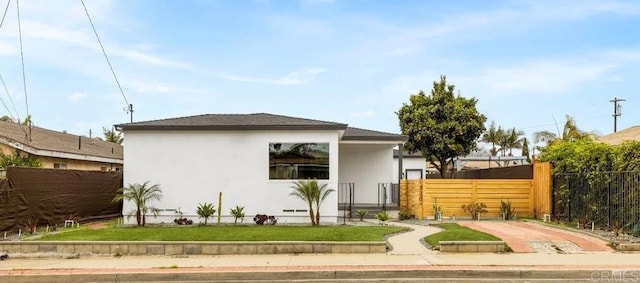 rear view of house with stucco siding and fence