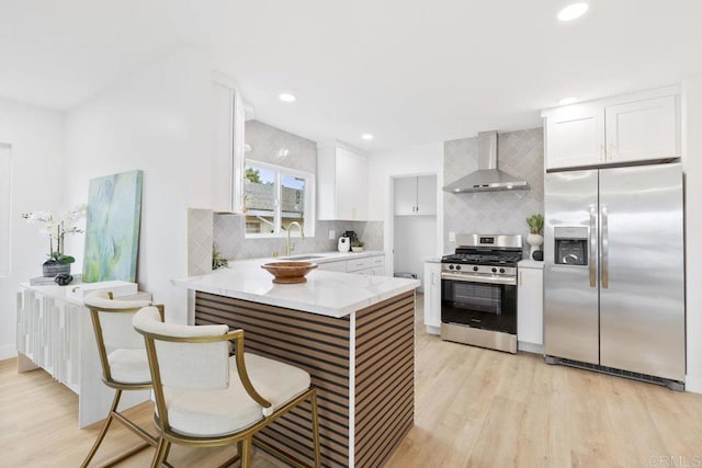 kitchen featuring light wood finished floors, stainless steel appliances, a sink, and wall chimney range hood