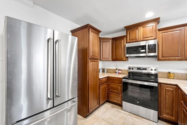 kitchen with stainless steel appliances, recessed lighting, brown cabinetry, light tile patterned flooring, and light stone countertops