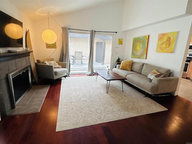 living room with high vaulted ceiling, dark wood-type flooring, and a tile fireplace