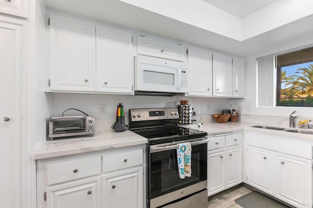 kitchen with stainless steel electric range oven, white microwave, a sink, white cabinets, and light wood-style floors