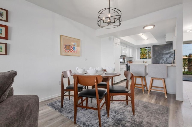 dining area with a raised ceiling, light wood-style flooring, baseboards, and a chandelier