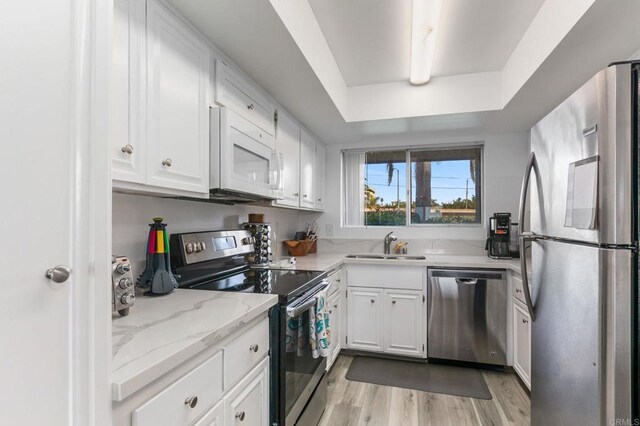 kitchen with a raised ceiling, white cabinets, appliances with stainless steel finishes, and a sink