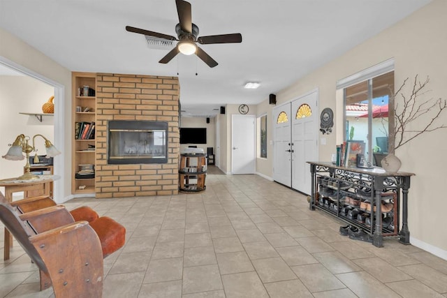 living area featuring light tile patterned floors, built in shelves, a ceiling fan, baseboards, and a brick fireplace