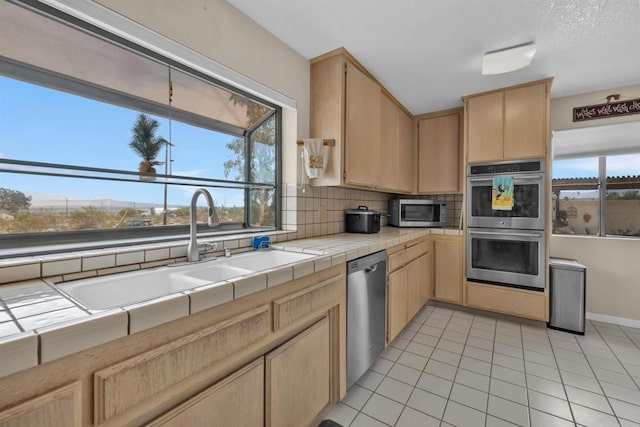 kitchen with appliances with stainless steel finishes, light brown cabinets, a sink, and tile countertops